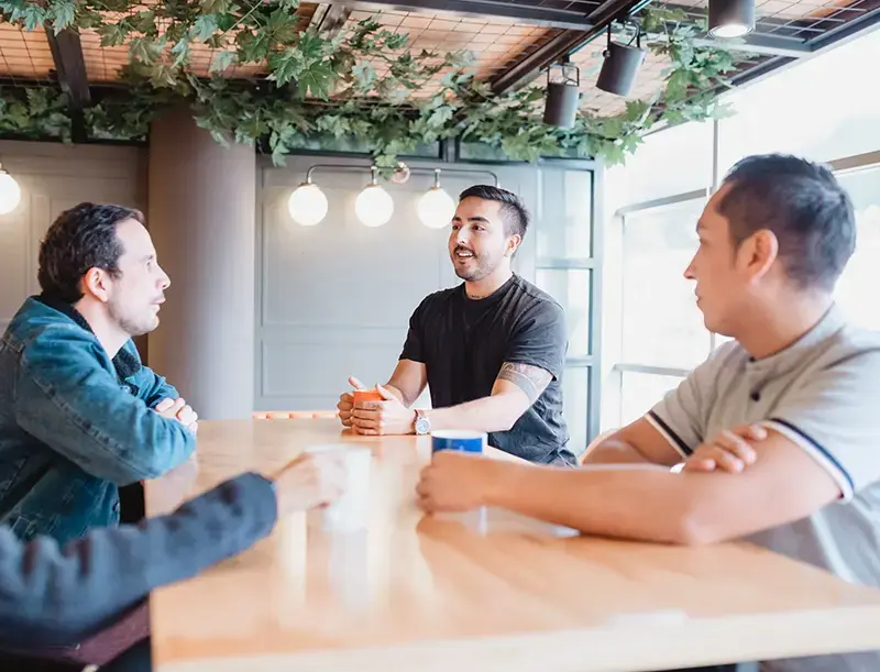 three male co-workers sit at coffee bar table