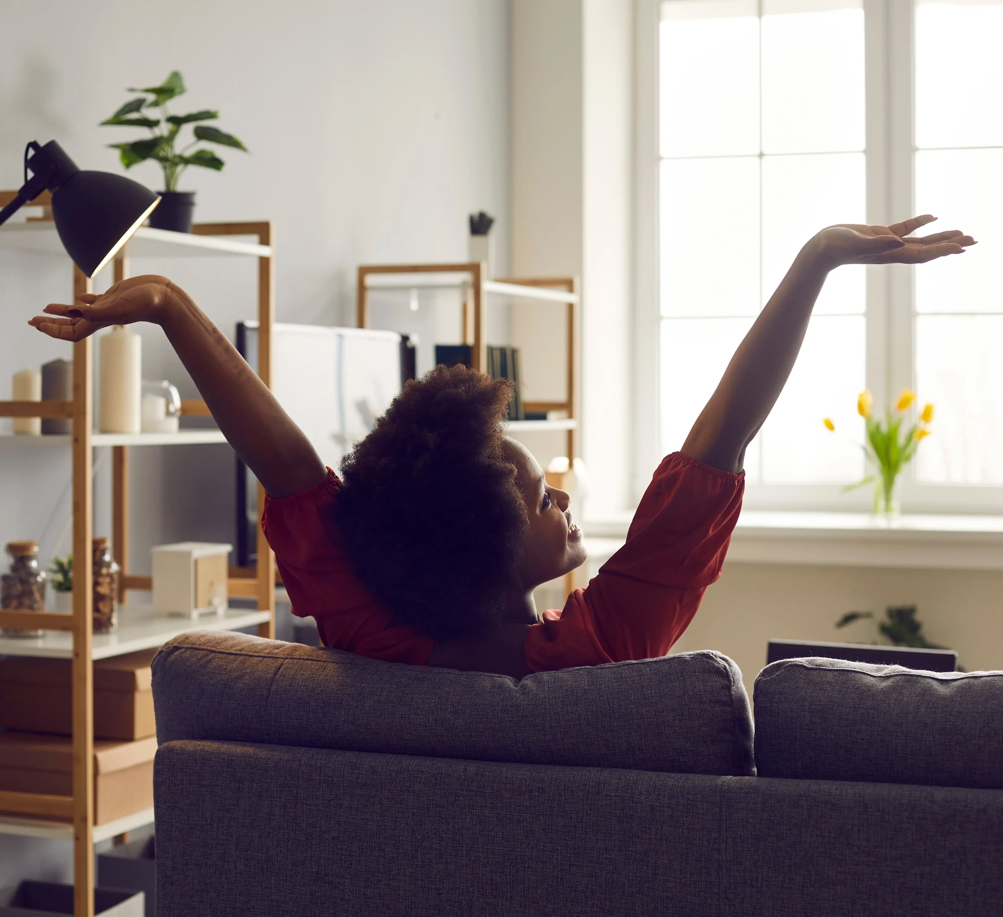 Happy woman on a couch with arms raised, embodying a sense of peace and wellness