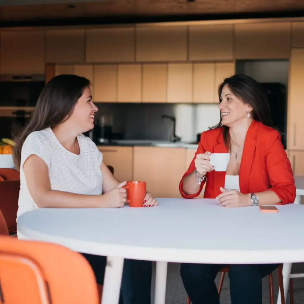 Two professionals enjoying a coffee break in a modern office kitchen, engaged in a friendly conversation.